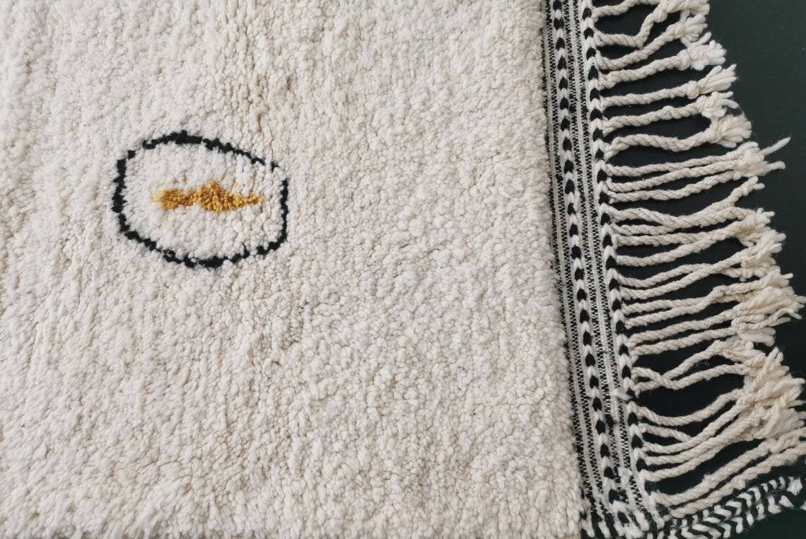 Detail close-up of a rug corner showing fringe and a soft texture in black and white.