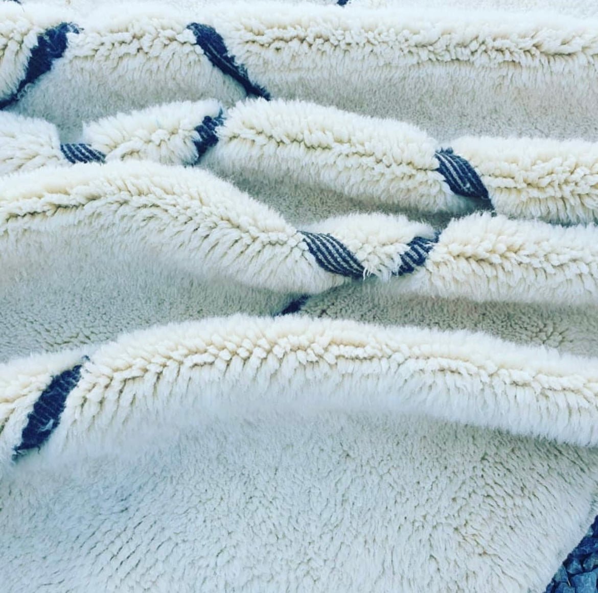 Lifestyle shot of a white Moroccan rug with geometric patterns and fringe edges in a natural setting.
