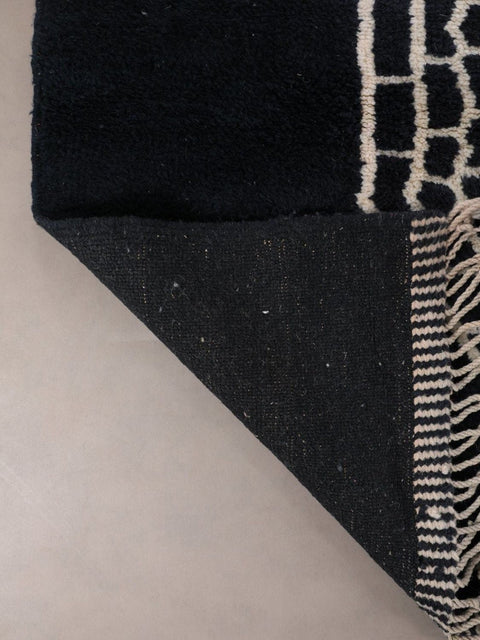 Close-up of a black and white rug with fringe edges and a thick pile.