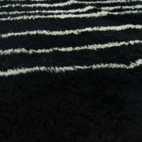 Close-up detail of a black area rug with a fringed edge and striped pattern.
