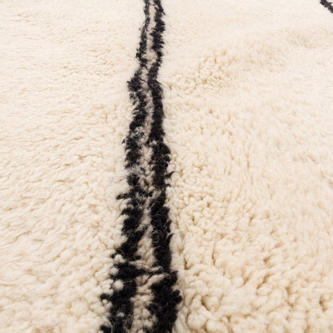 Texture detail showing soft fibers and curled edge of the beige striped Moroccan rug.