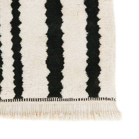 Close-up detail of the black and cream striped Beni Ourain Moroccan rug featuring a zigzag pattern and fringe edges.