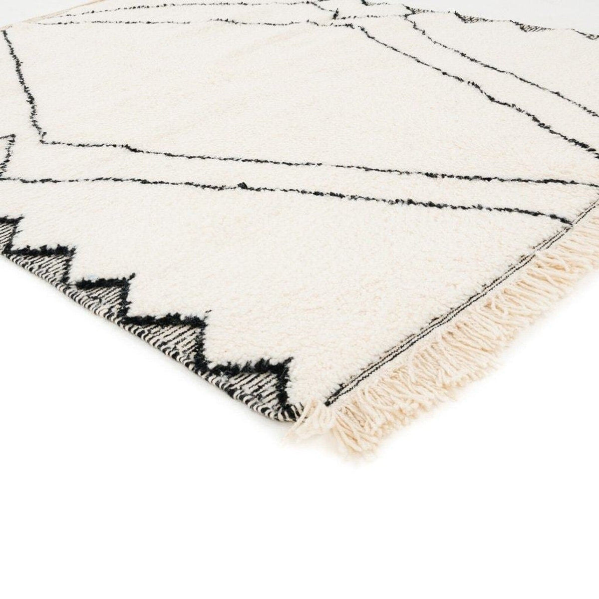 Close-up detail of the black and white Moroccan rug featuring geometric patterns and fringe edges.