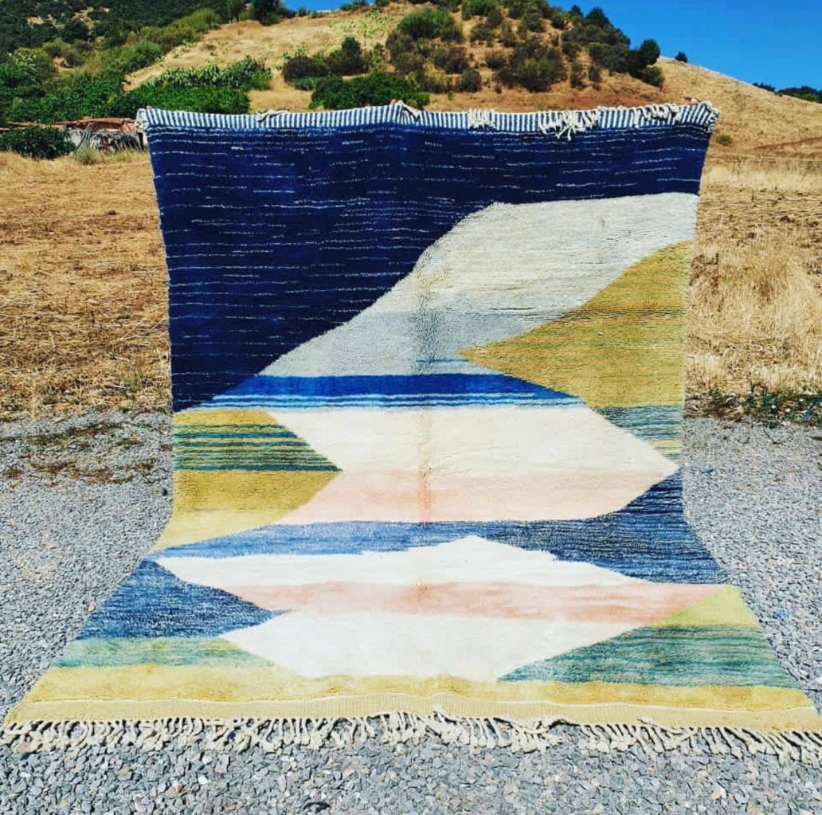 Lifestyle shot of a blue and yellow geometric Moroccan Berber rug with a natural background.