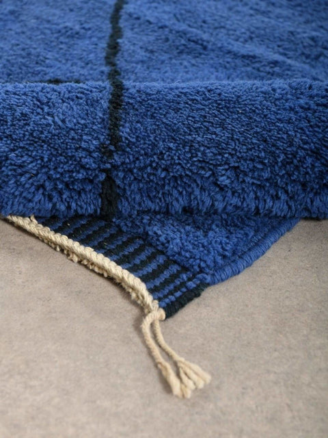 Detail close-up of the edge of the blue diamond rug featuring fringe detail.