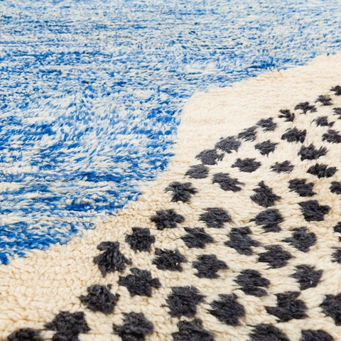 Side view of the blue, cream, and orange abstract Moroccan rug highlighting its soft texture.