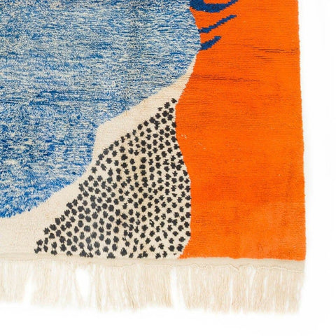 Close-up detail of the blue and orange rug with fringe edges and bold design.