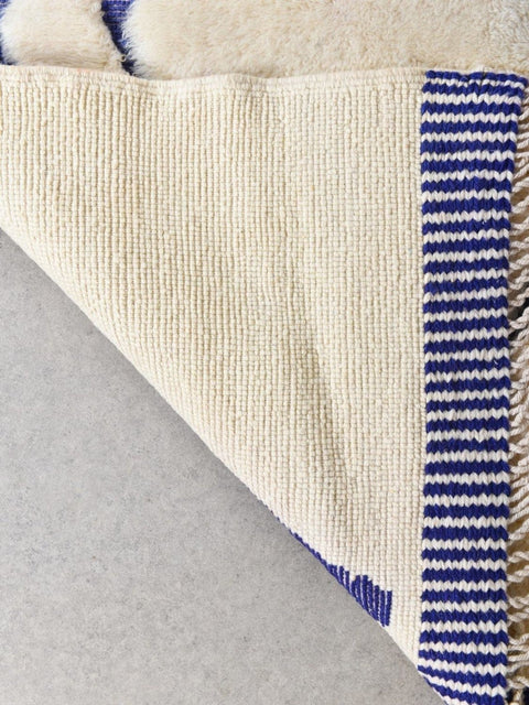 Detail view of the fringed edge and woven texture of a blue and cream rug.