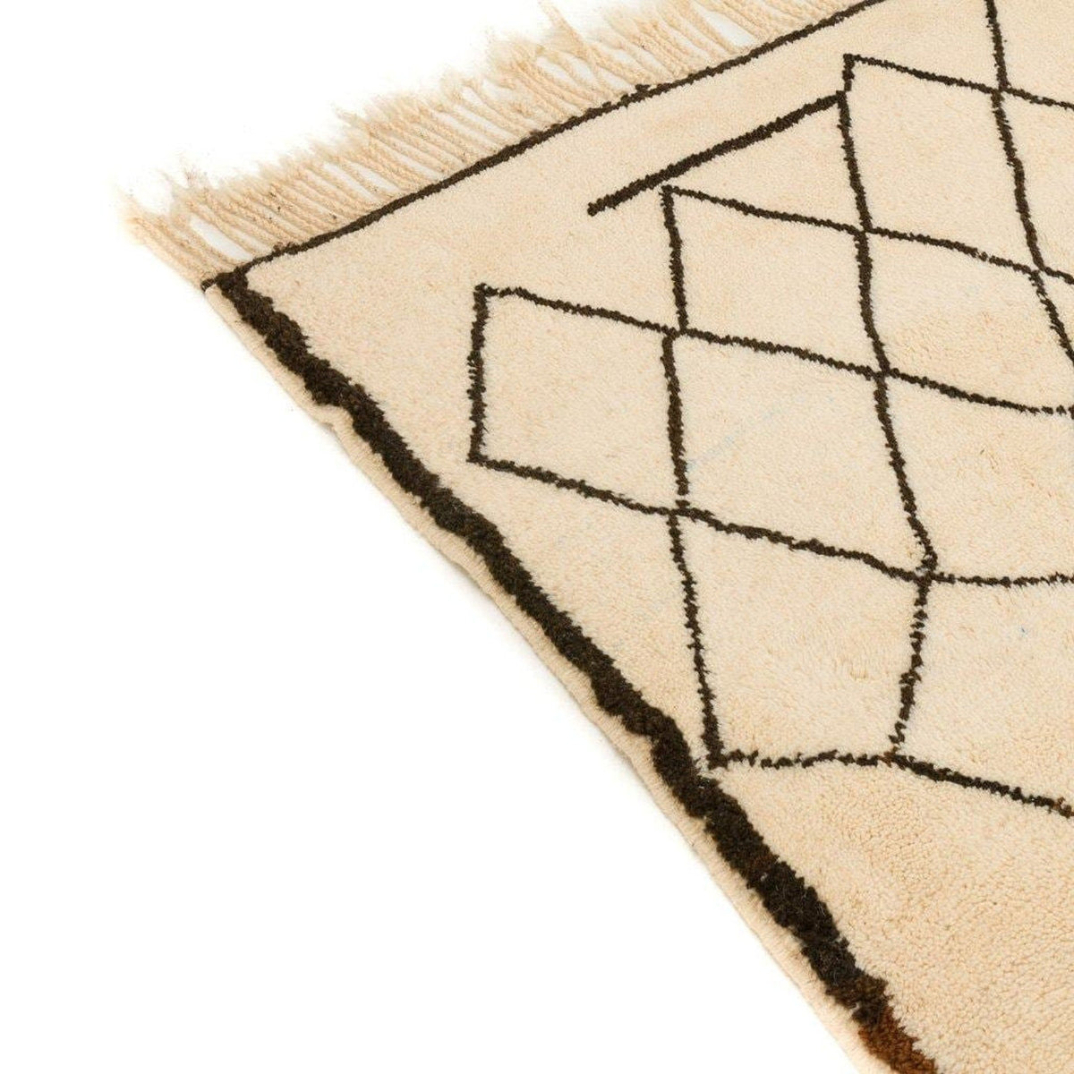 Detail close-up of the edge of the cream Beni Ourain Moroccan rug highlighting frayed edges and geometric lines.