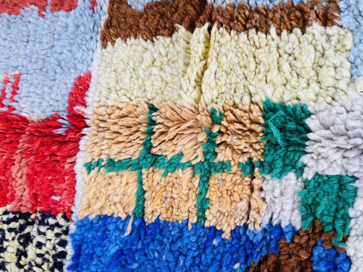 Close-up detail of a colorful woven rug showing a textured pattern in red, brown, green, and beige.