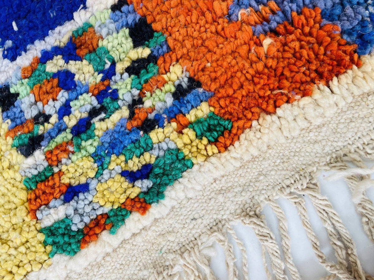 Close-up detail of textured rug fibers displaying orange, green, blue, and cream colors.