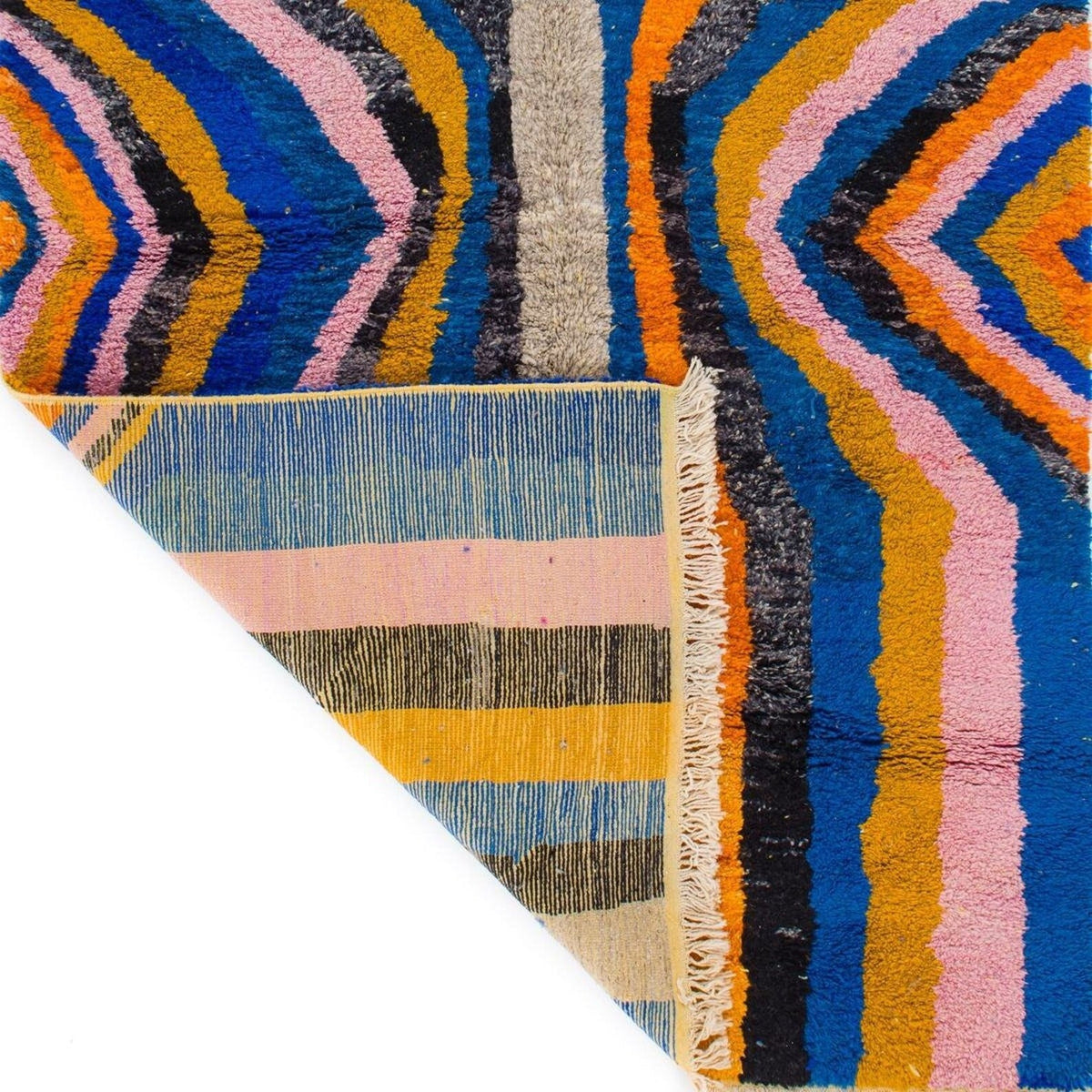 Detail view of a colorful rug with a geometric pattern and fringed edge.