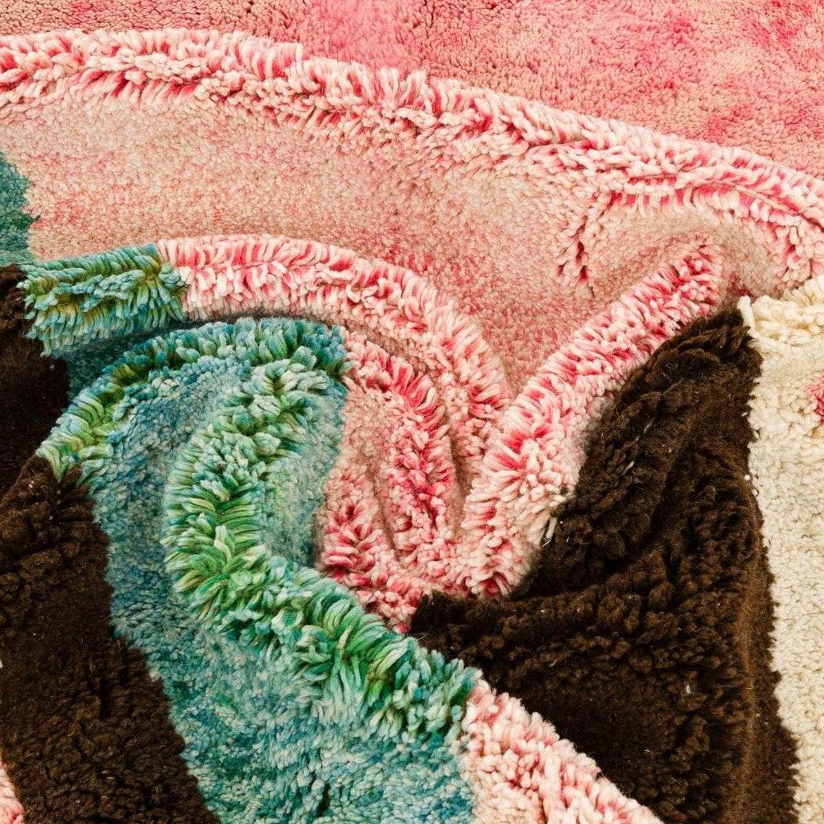 Close-up detail of a colorful Moroccan rug featuring layered textures and fringe edges in pink, brown, green, and cream.