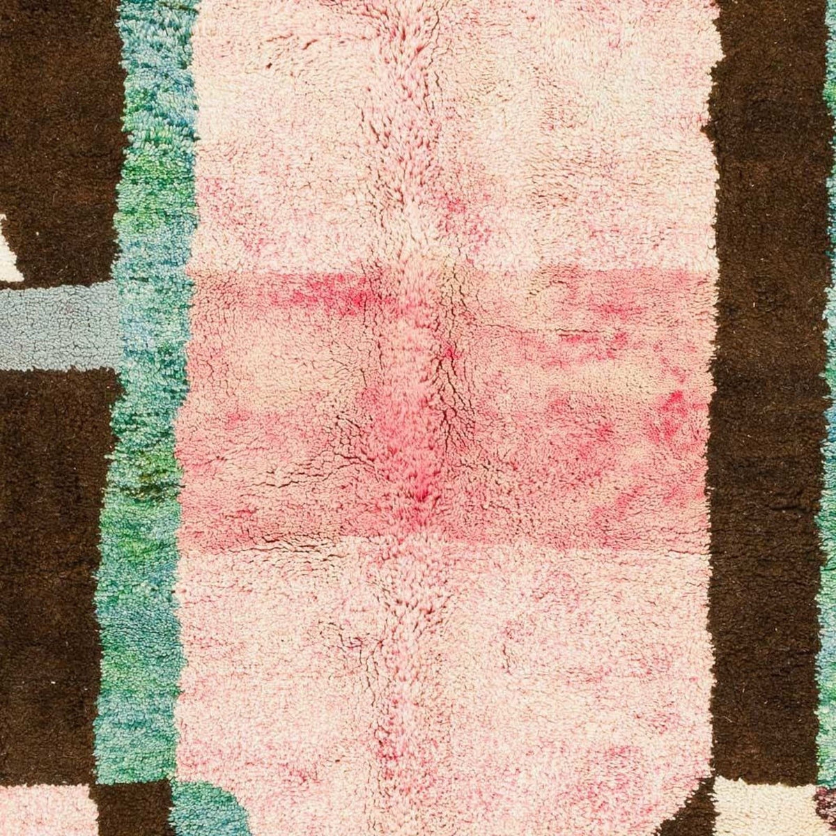Close-up detail of a colorful Moroccan rug showcasing abstract patterns and fringe edges in pink, brown, green, and cream.