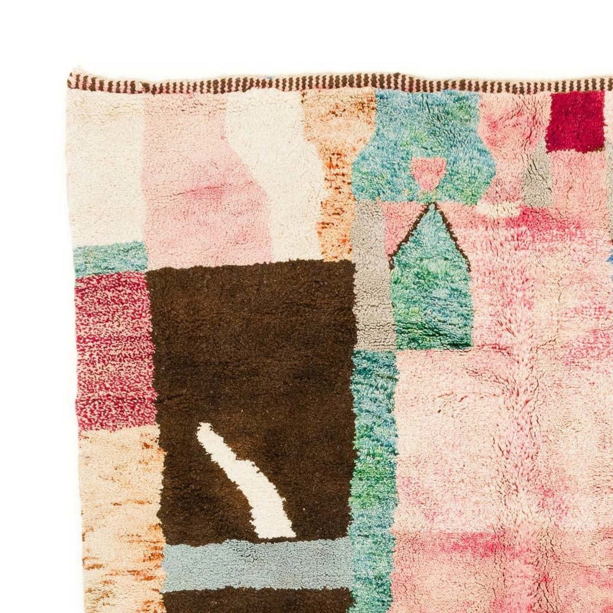 Close-up detail of a colorful Moroccan rug with patchwork design and fringe edges in pink, brown, blue, and cream.