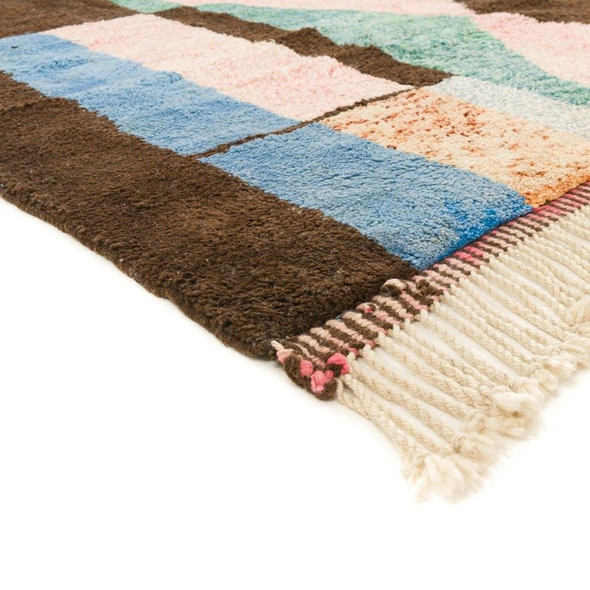 Close-up detail of a Moroccan rug displaying faded colors and fringe edges in brown, blue, pink, and cream.
