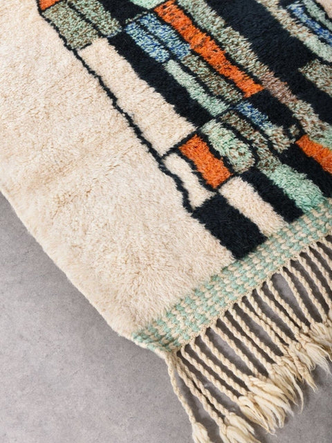 Detail shot of the abstract wool rug showcasing a colorful design in black, orange, green, and beige.