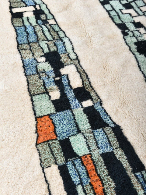 Detail shot of the abstract wool rug featuring a textured surface with colorful blocks in black, blue, orange, and beige.