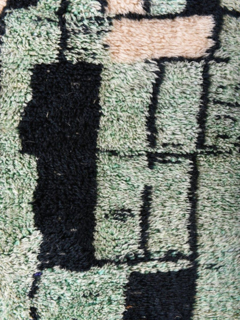 Detail shot of the abstract wool rug featuring a geometric pattern in black, green, and beige.