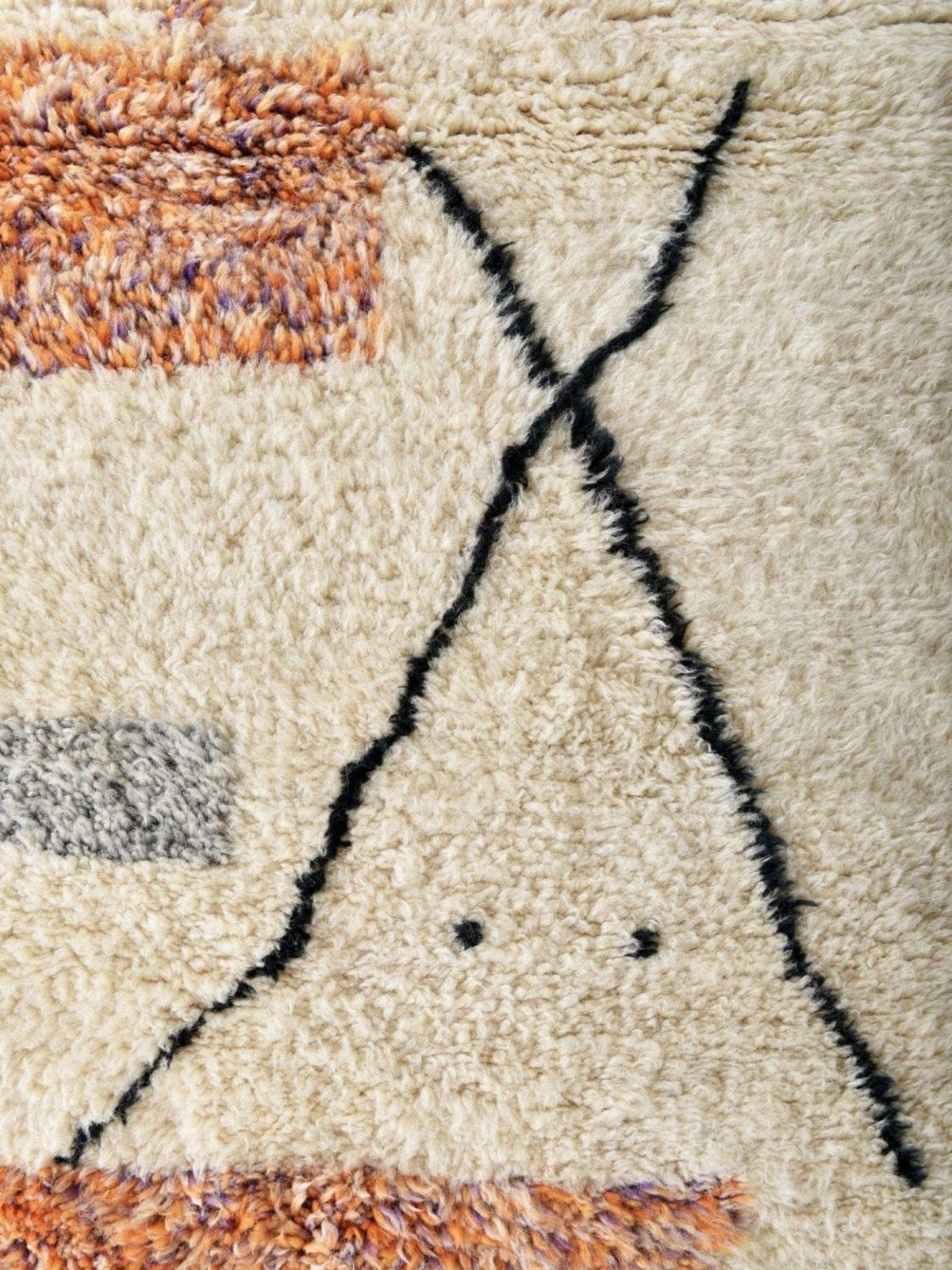 Detail close-up of a cream and orange area rug with an artistic pattern and fringe detail.