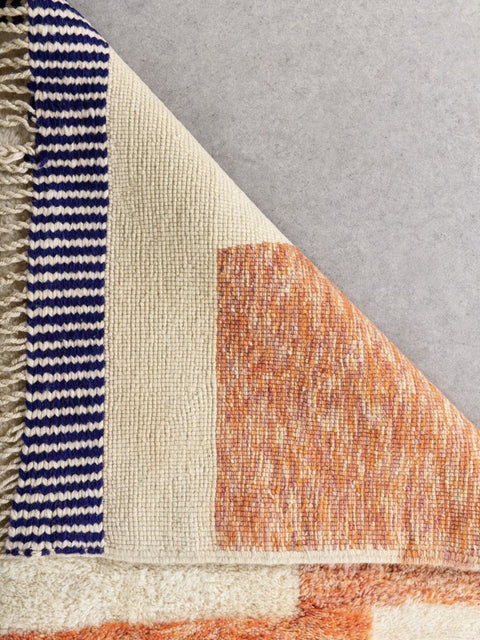 Detail close-up of a cream and blue geometric area rug featuring fringe edges.
