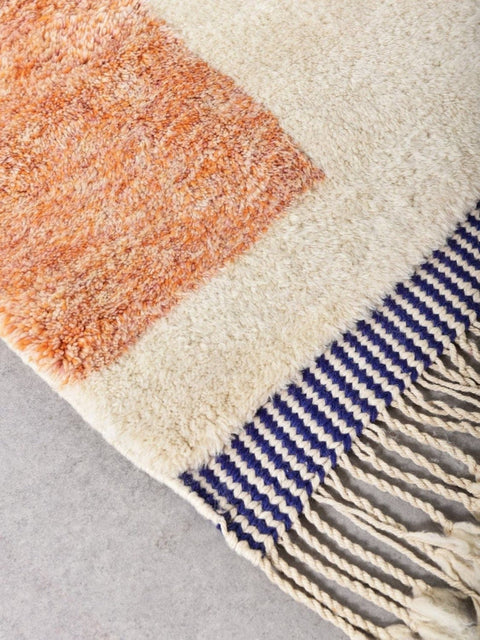 Detail close-up of a cream and orange abstract wool rug with fringe detail.