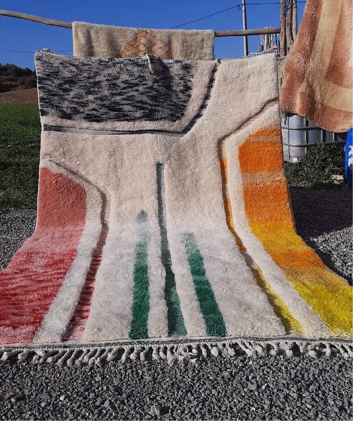 Lifestyle shot of a colorful Berber rug featuring geometric patterns in beige, orange, green, and red.