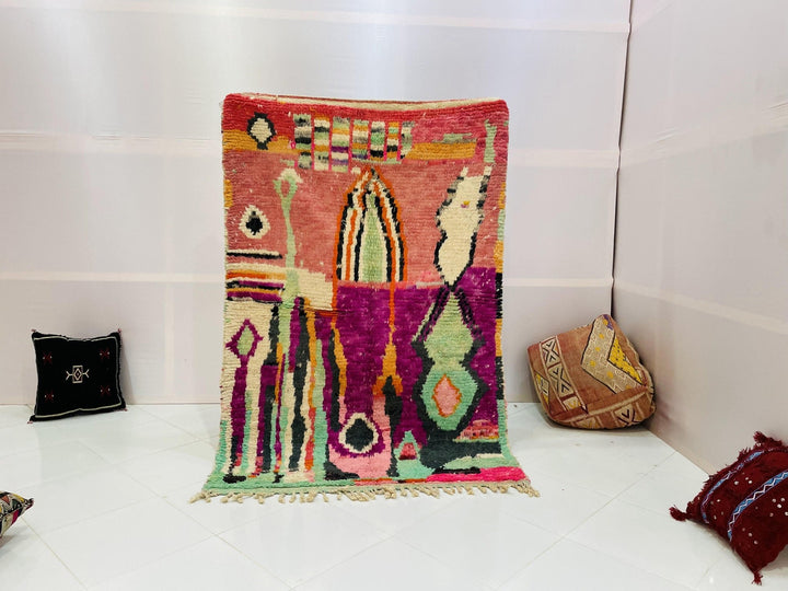 Lifestyle shot of a vintage Moroccan rug featuring geometric patterns in red, green, pink, and yellow.