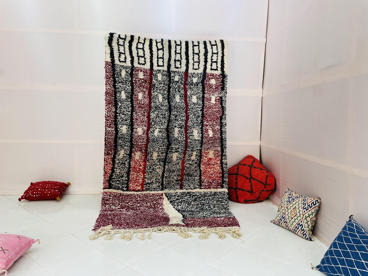 Lifestyle shot of a pink geometric Moroccan rug with red and black patterns in a studio setting.