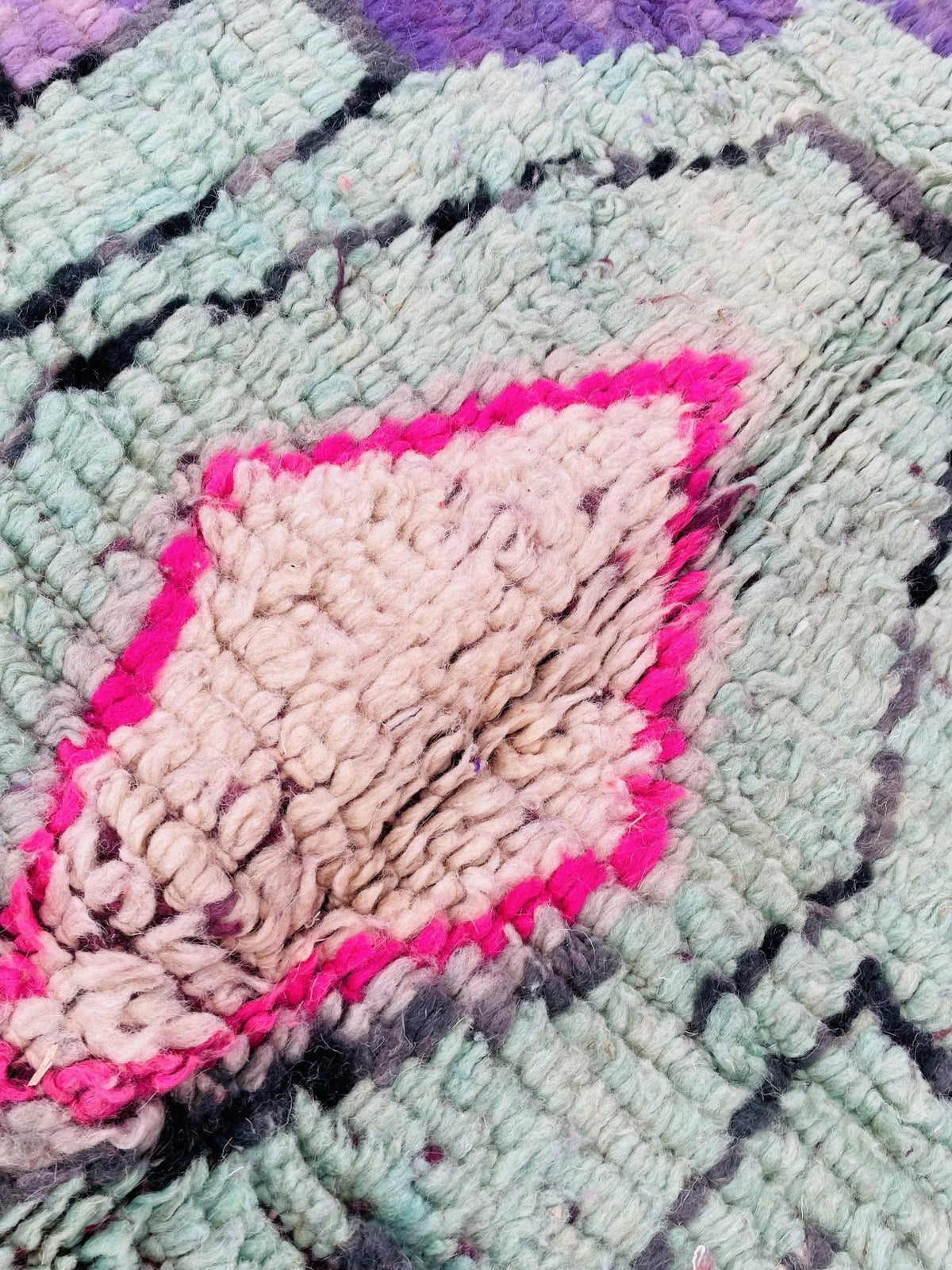 Close-up detail of a vintage Moroccan rug featuring abstract patterns in purple, pink, and white.