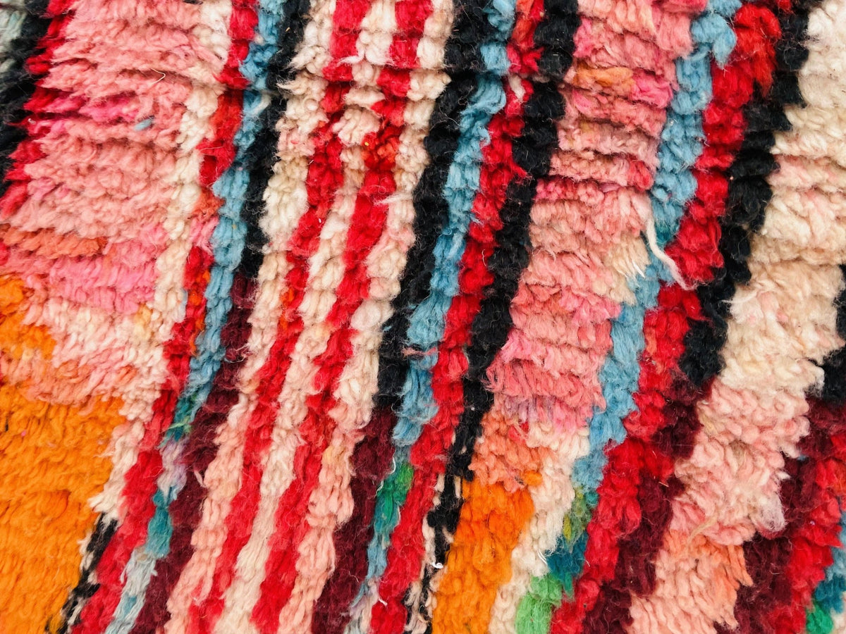 Close-up detail of a vintage Moroccan rug displaying a striped pattern with red, orange, black, and white.