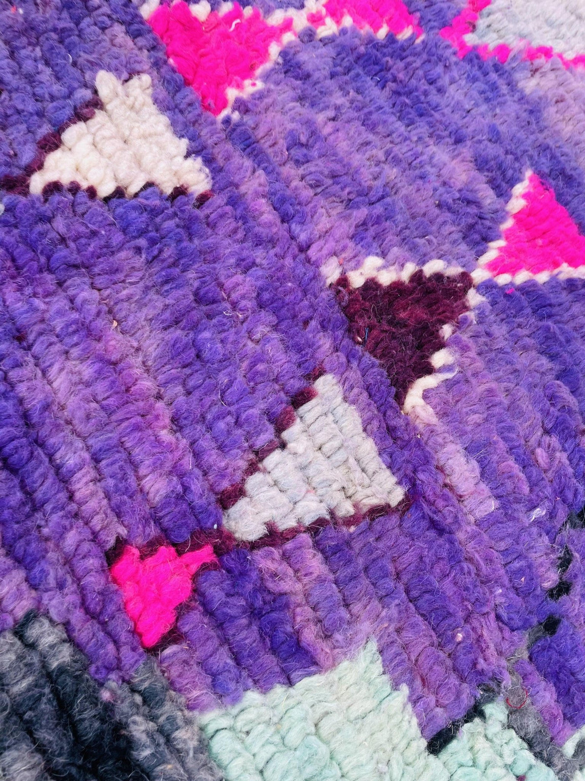 Close-up detail of a vintage Moroccan rug displaying abstract patterns in purple, pink, and white.
