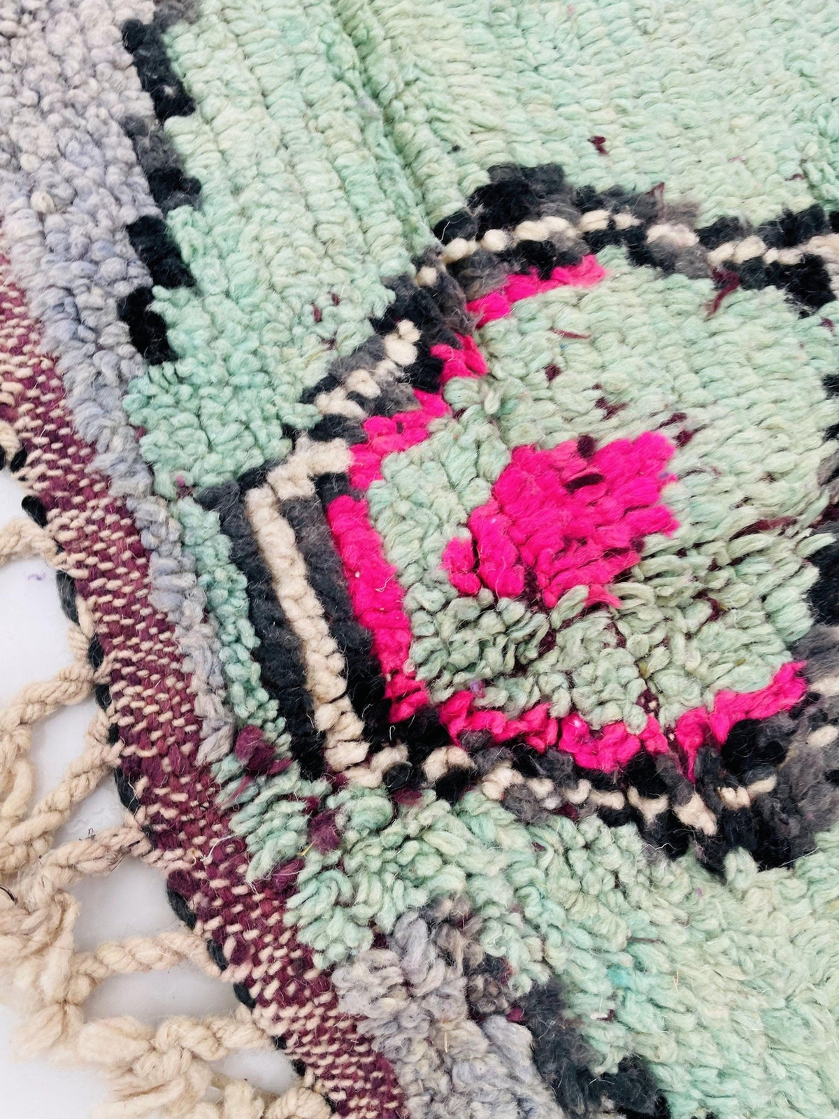 Lifestyle shot of a large vintage Moroccan rug with abstract design and fringe edges in purple, green, and pink.