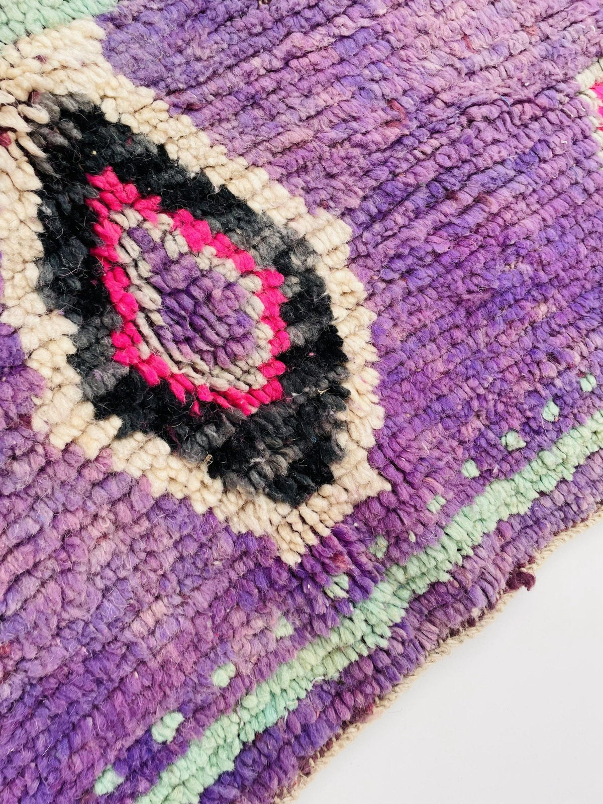 Close-up detail of a vintage Moroccan rug with geometric shapes in purple, black, and pink.