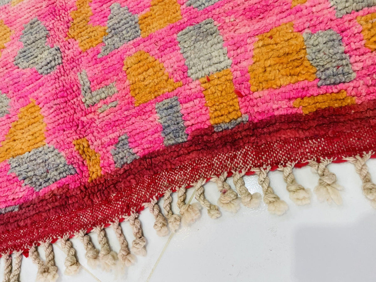 Close-up detail of the woven texture of a pink Moroccan rug with colorful patterns.