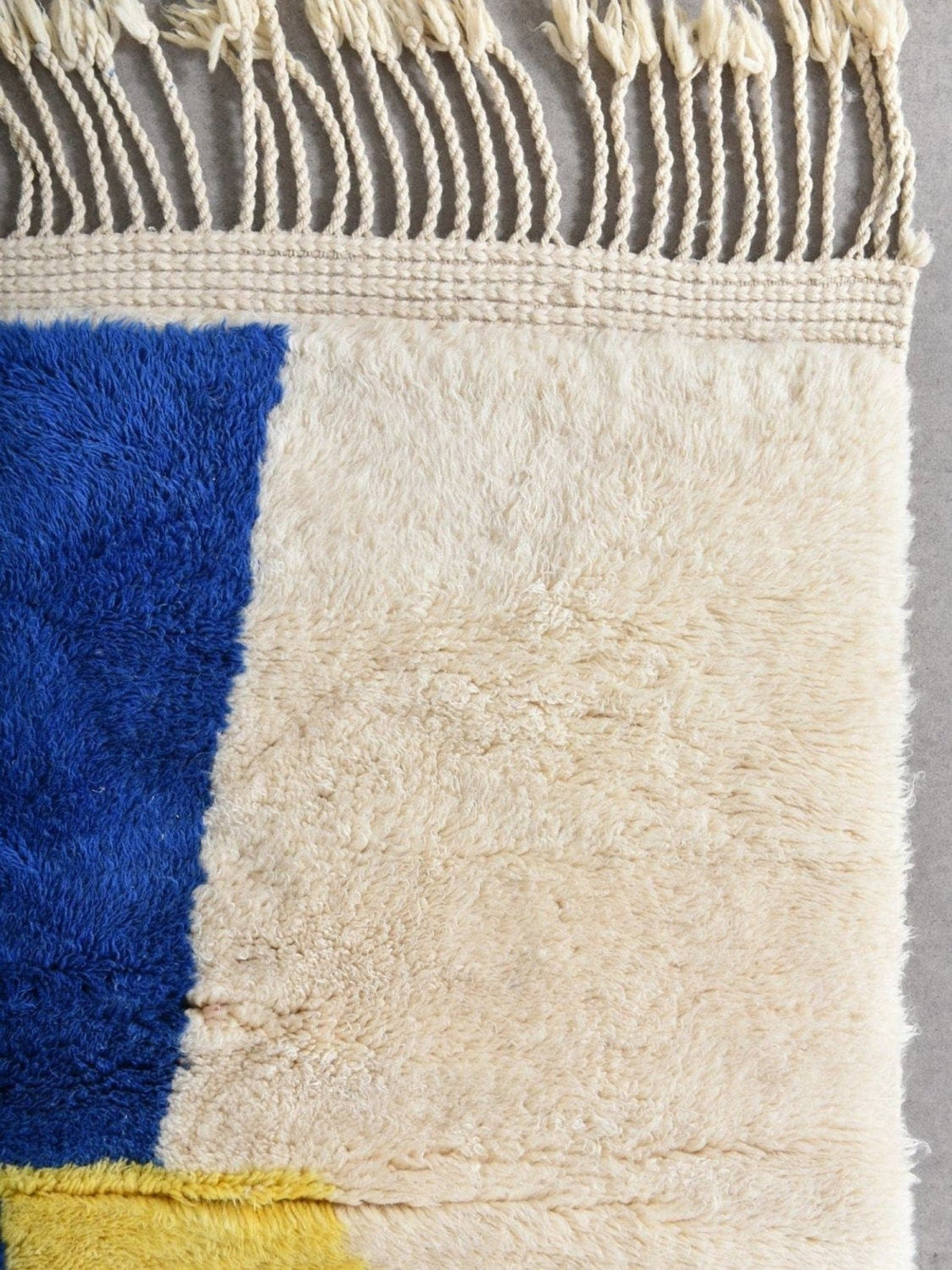 Detail view of the abstract wool rug in beige and blue with textured surface and fringe edges.