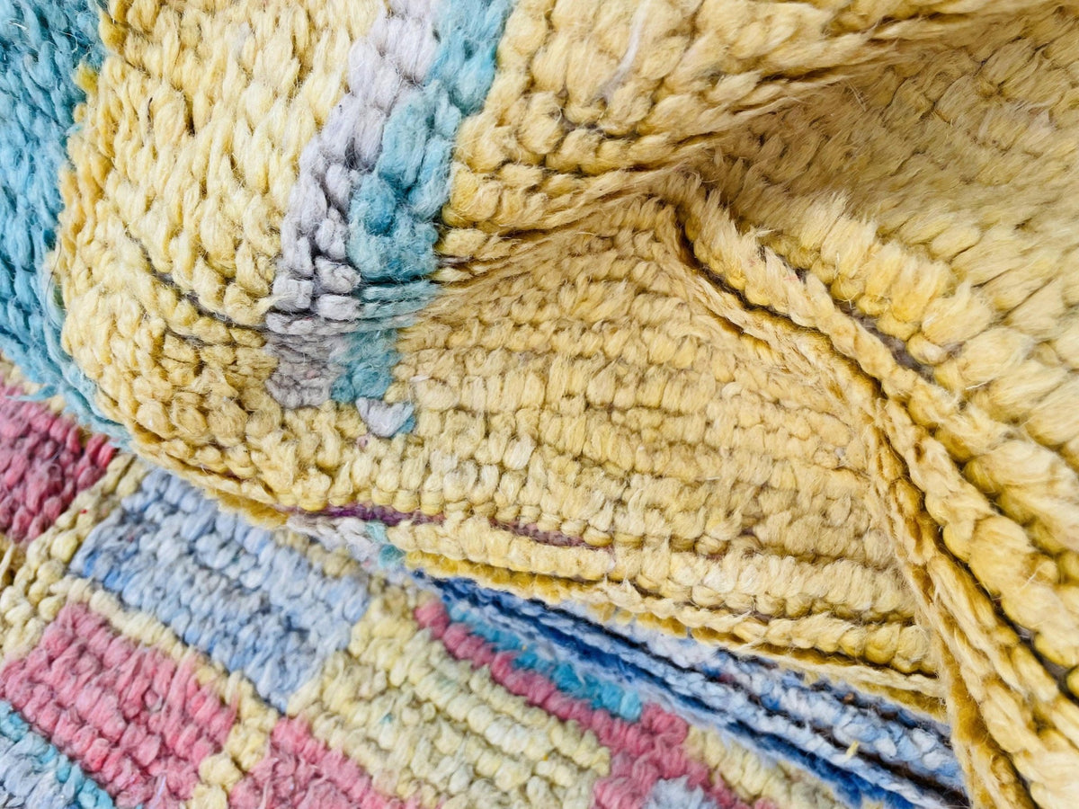 Lifestyle view of a vintage Moroccan rug with yellow and red colors displayed on a white surface.