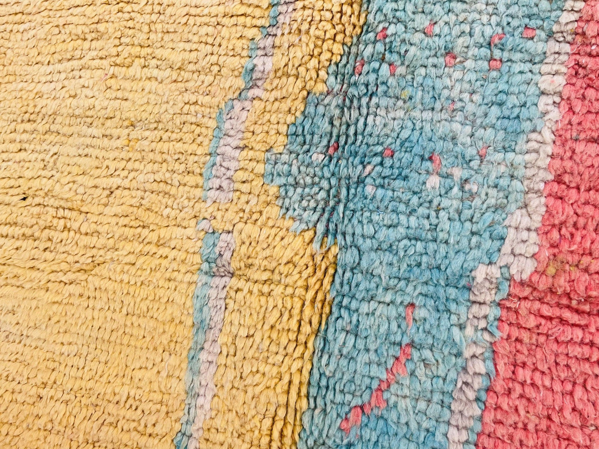 Close-up detail of a vintage Moroccan rug showcasing red, yellow, and blue colors in a textured view.