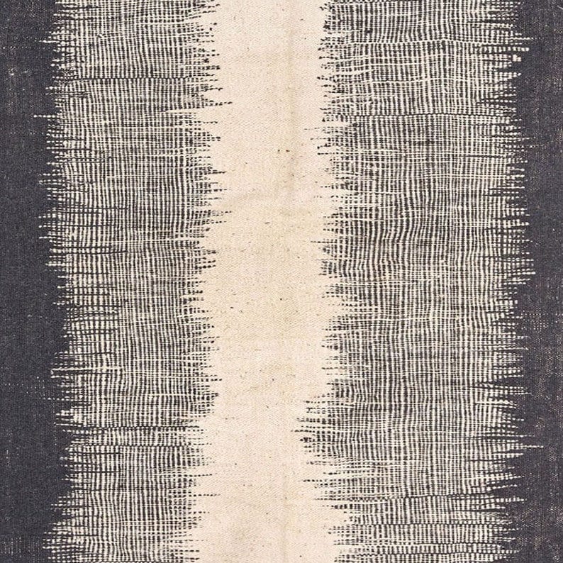 Close-up detail of the woven texture on the black, gray, and cream striped Kilim rug.