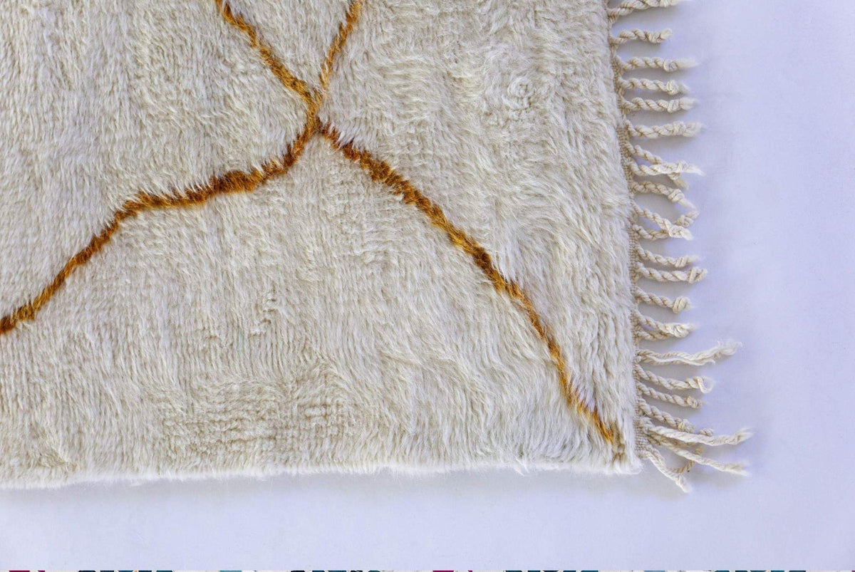 Detail view of the fringed edge with a gold pattern on the abstract rug.