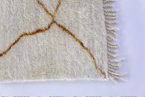 Detail view of the fringed edge with a gold pattern on the abstract rug.