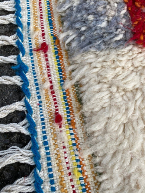 Side view of a colorful Moroccan rug showcasing geometric patterns and fringed edges.