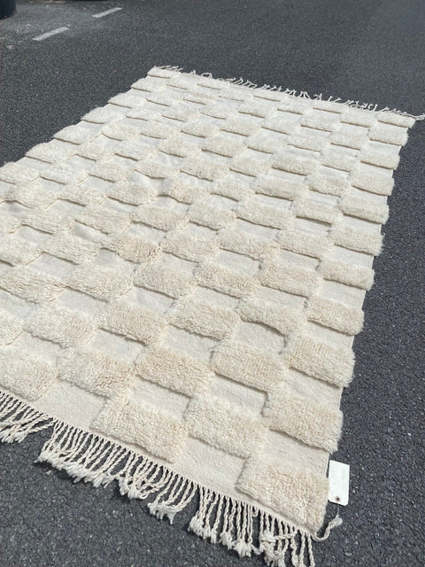 Detail close-up of a checkered Moroccan rug with fringed edges in white and beige.