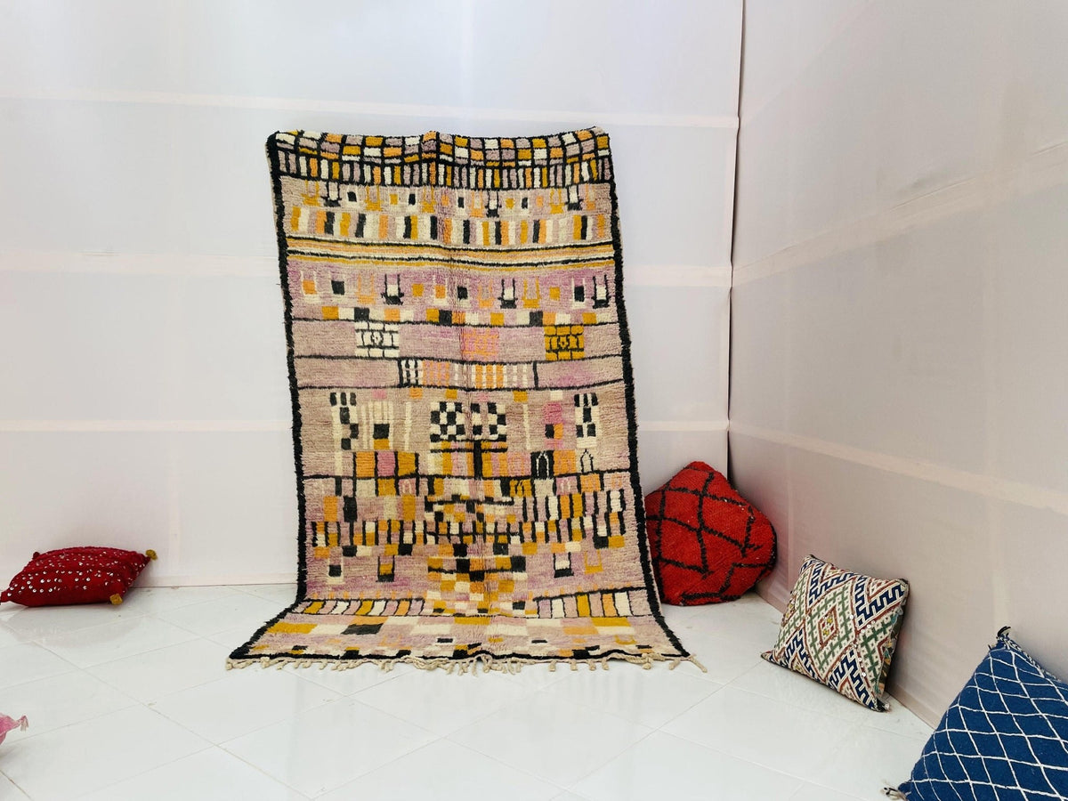 Lifestyle shot of a pink abstract Moroccan rug with geometric patterns on a white background.