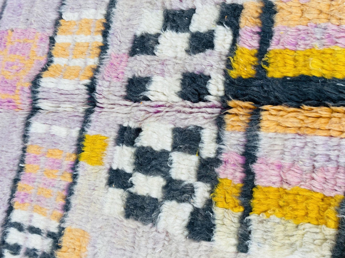 Close-up view of geometric patterns in yellow and purple on a pink abstract Moroccan rug.