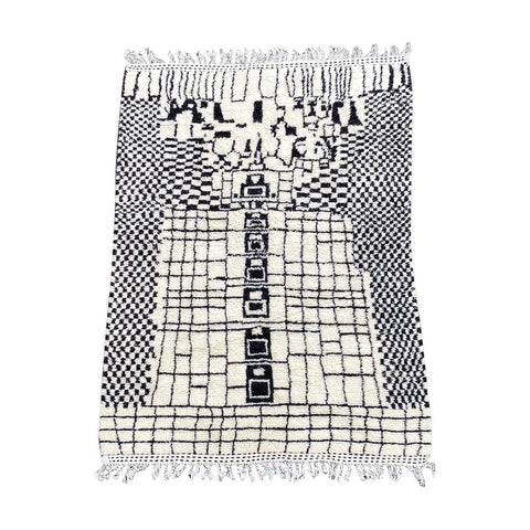 Lifestyle shot of a black and white geometric rug with fringe edges on a natural background.