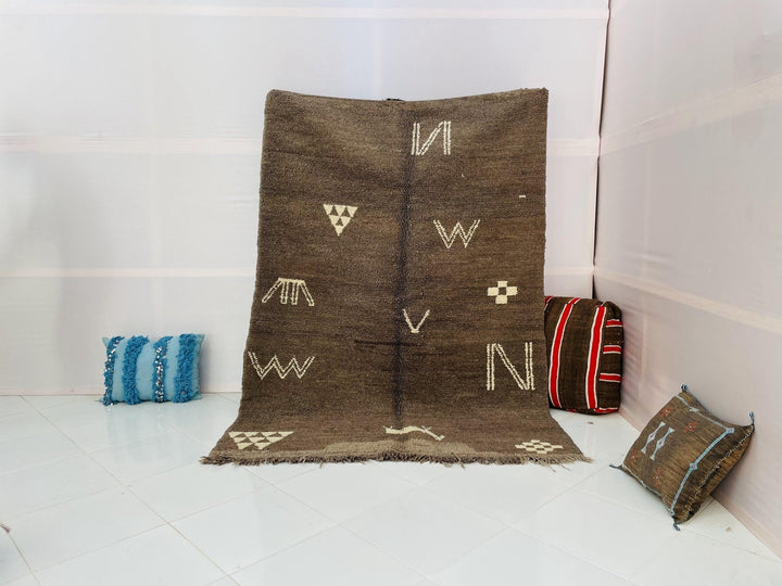 Lifestyle shot of a grey and brown vintage Moroccan rug with abstract patterns and fringe edges.