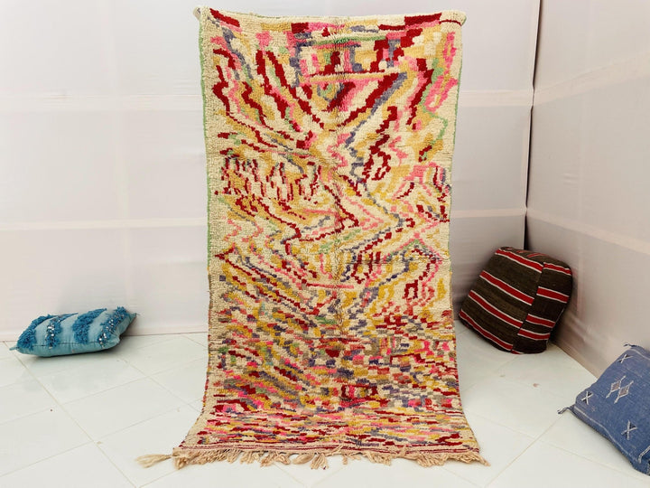 Lifestyle shot of a cream and red abstract vintage Moroccan rug with fringe edges on a white background.