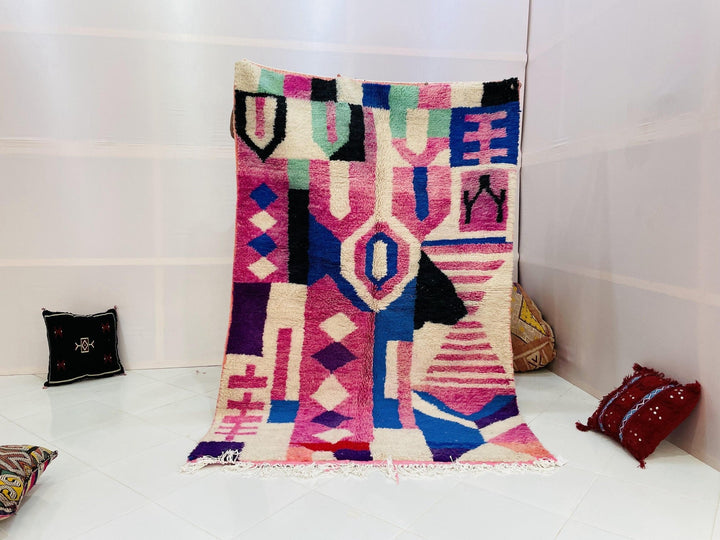 Lifestyle shot of a vintage Moroccan rug featuring geometric patterns in pink and blue.