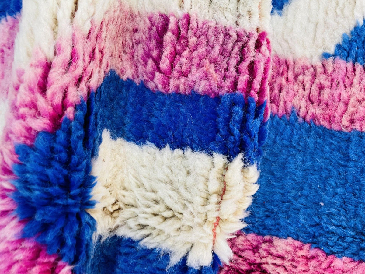 Lifestyle image of a vintage Moroccan rug with geometric patterns in pink and blue colors.